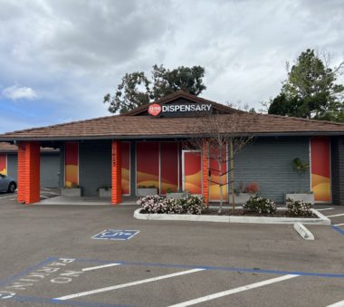 A single-story building with a brown roof and colorful red and orange wall panels under a cloudy sky