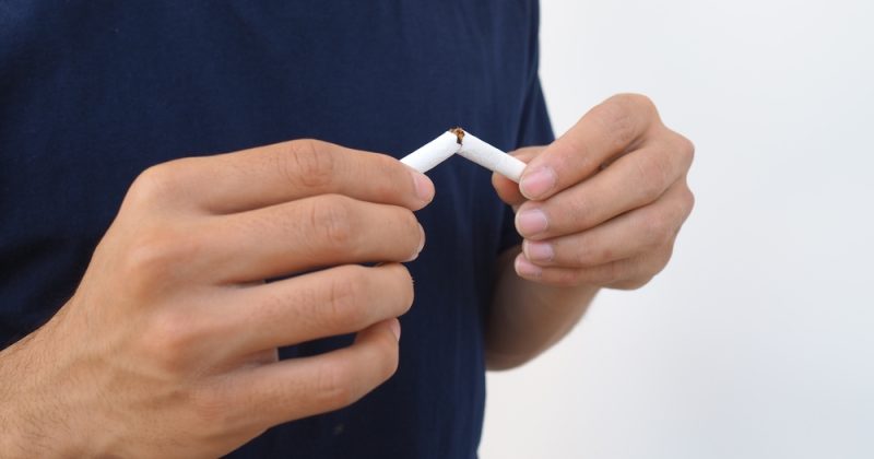 Person breaking a cigarette in half against a plain white background.