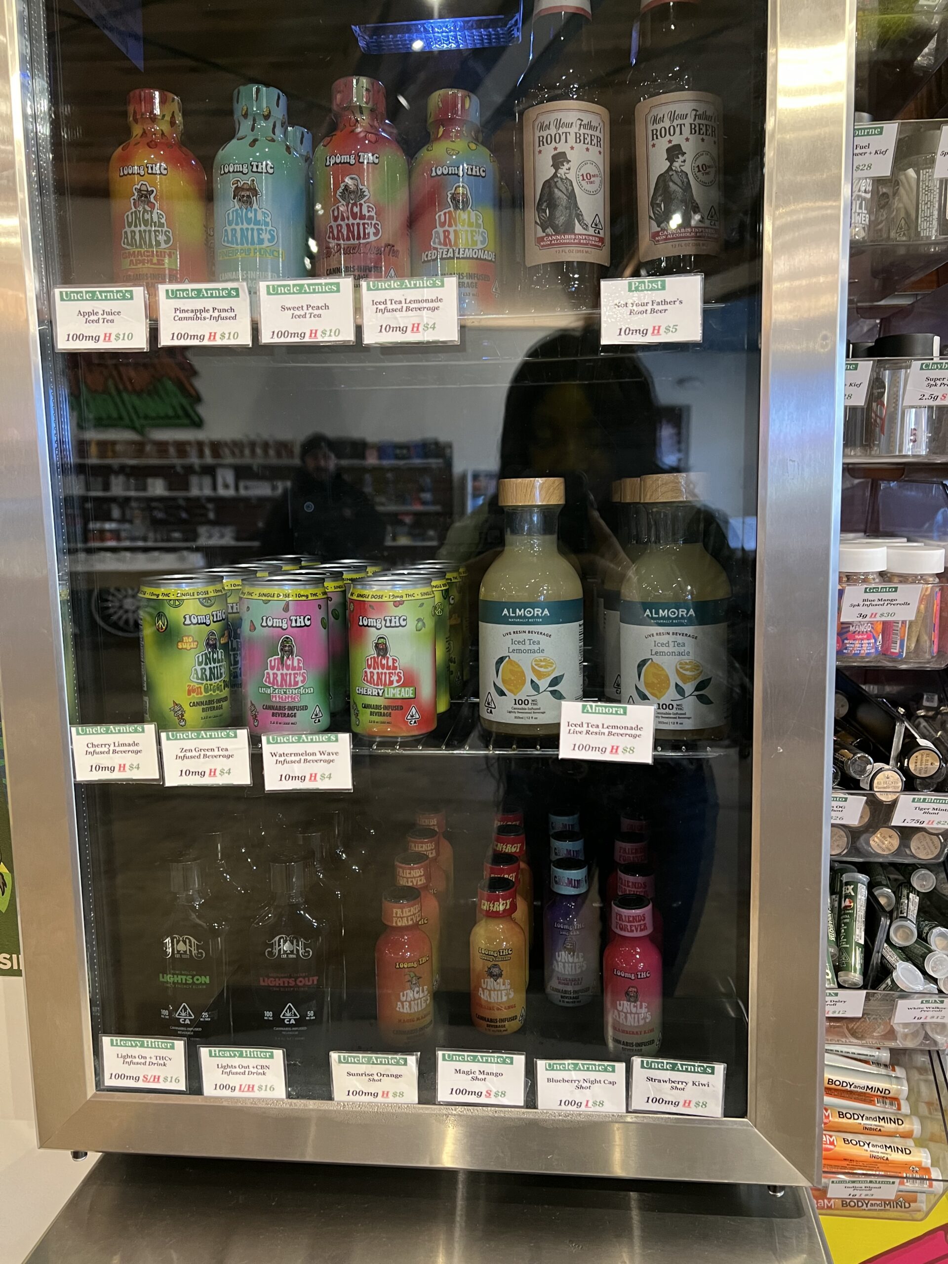 Refrigerated shelf displaying various bottled and canned beverages with visible price tags