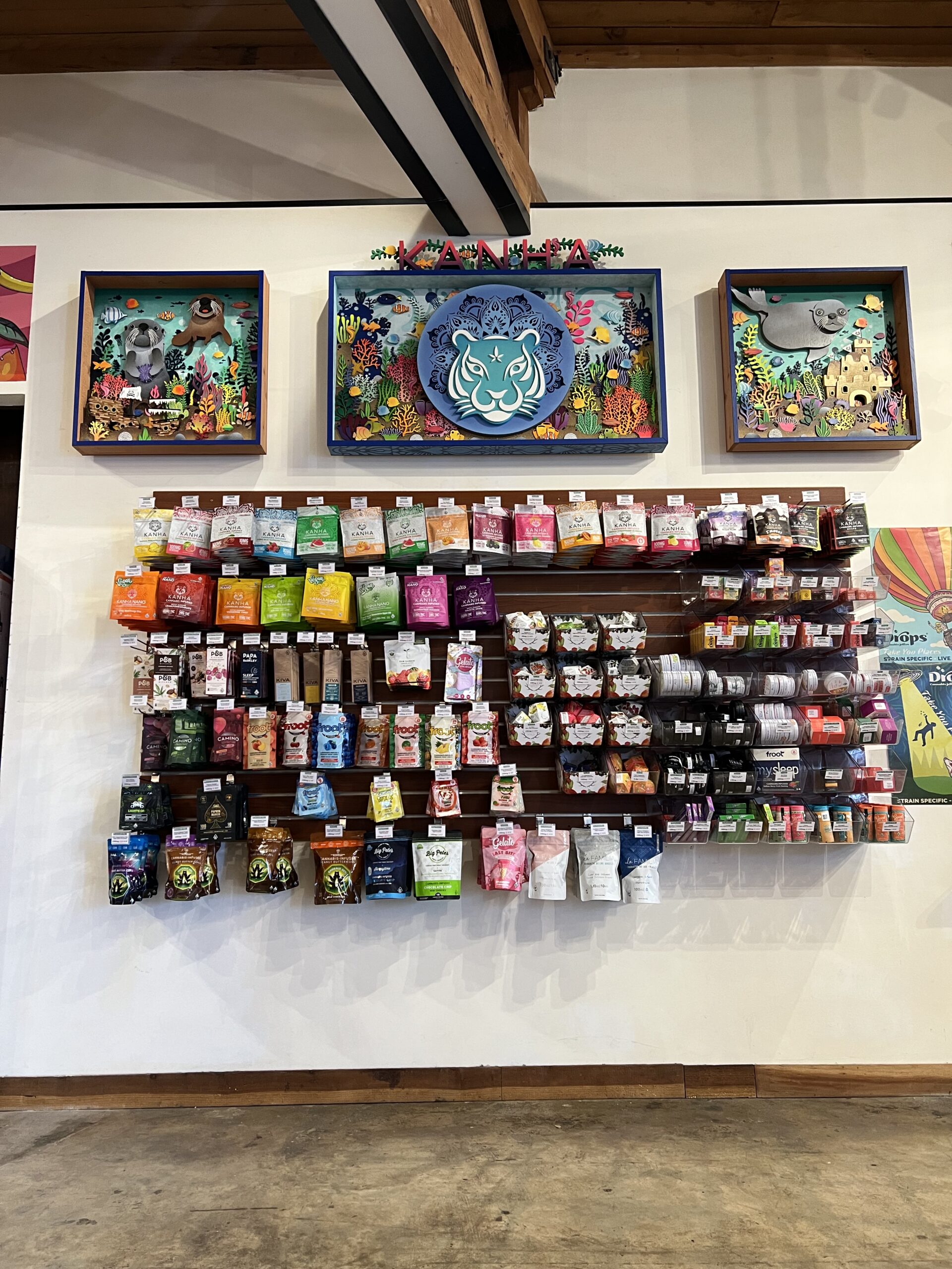 Wall display of various packaged cannabis products arranged neatly beneath three colorful animal-themed shadow box artworks
